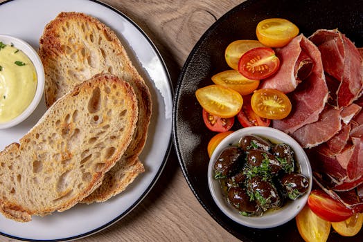 Assiette d'apéritif avec pain grillé, tapenade, tomates cerises et charcuterie sur une table en bois.