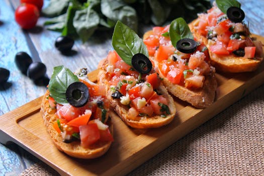 Bruschettas garnies de tomates, olives et basilic sur une planche en bois, avec des ingrédients frais en arrière-plan.