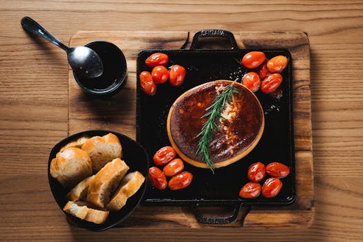 Plateau en bois avec pain, tomates cerises rôties et fromage crémeux, décoré d'une branche de romarin.