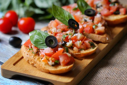 Tartines garnies de tomates, olives et basilic sur une planche en bois, avec des tomates cerises en arrière-plan.